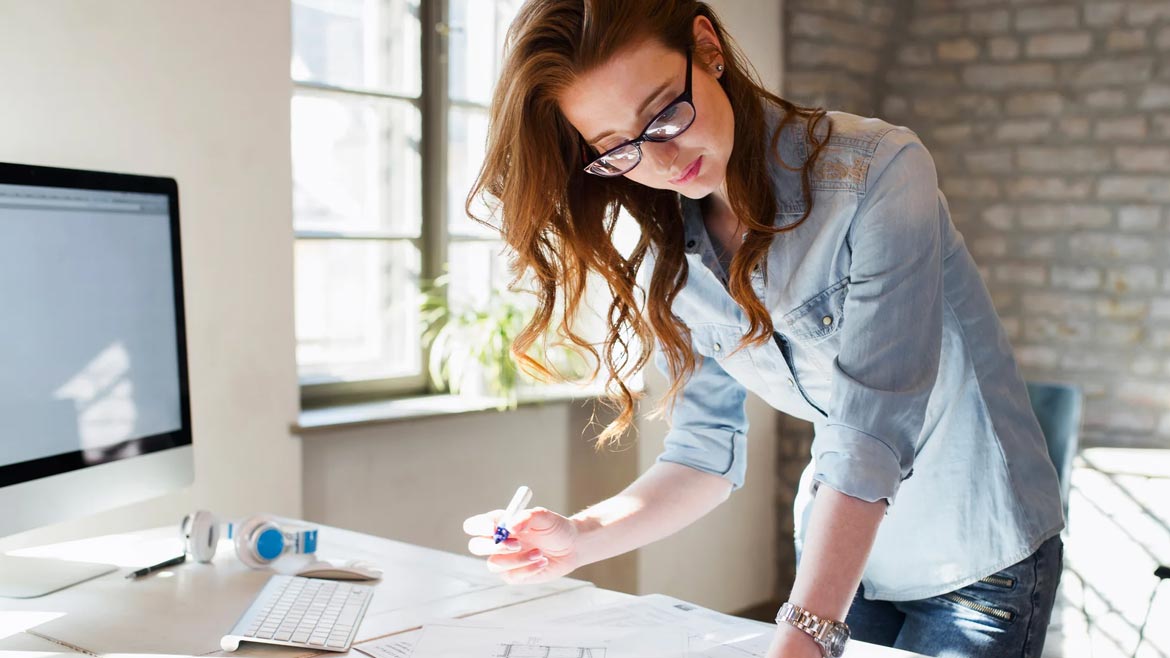 Figure 2 of woman standing by her desk with desktop computer, working