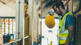 Worker leaning, wiping sweat off forehead, holding his safety hat in his hands.