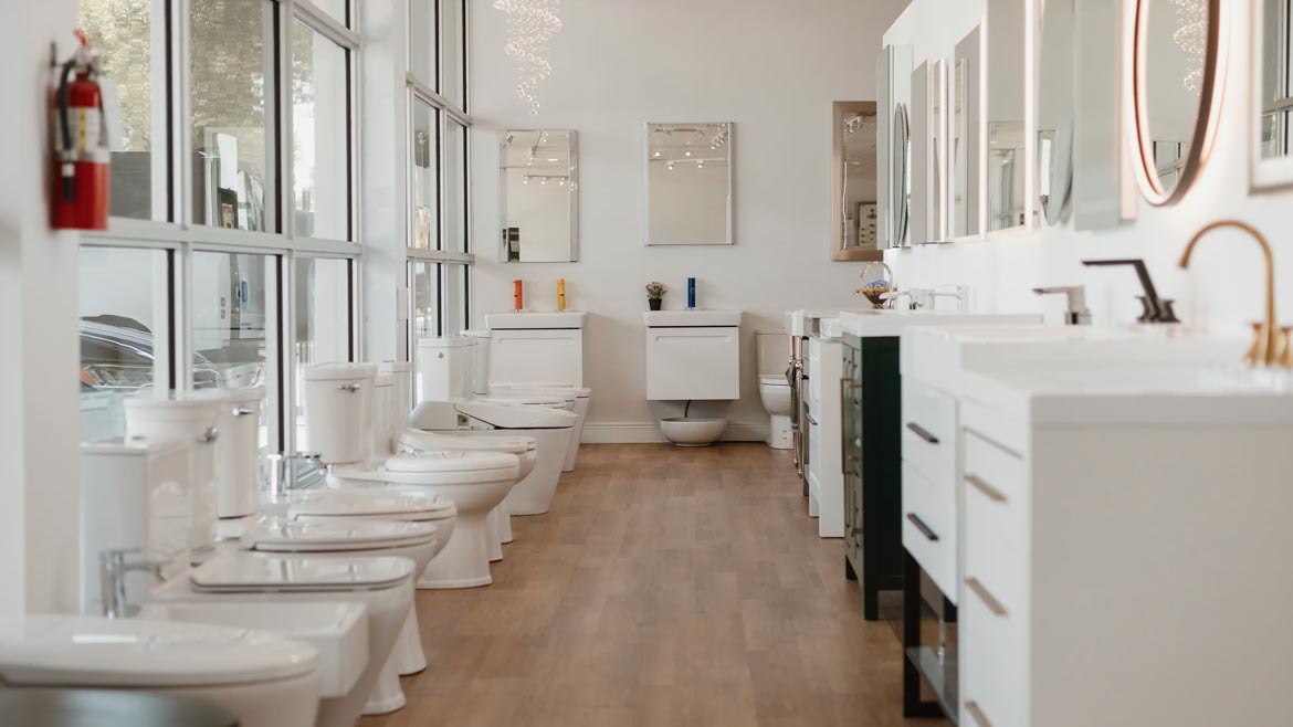 The Kitchen + Bath Design Studio by Lion Plumbing Supply showing a row of toilets on the left and bathroom vanities on the right.