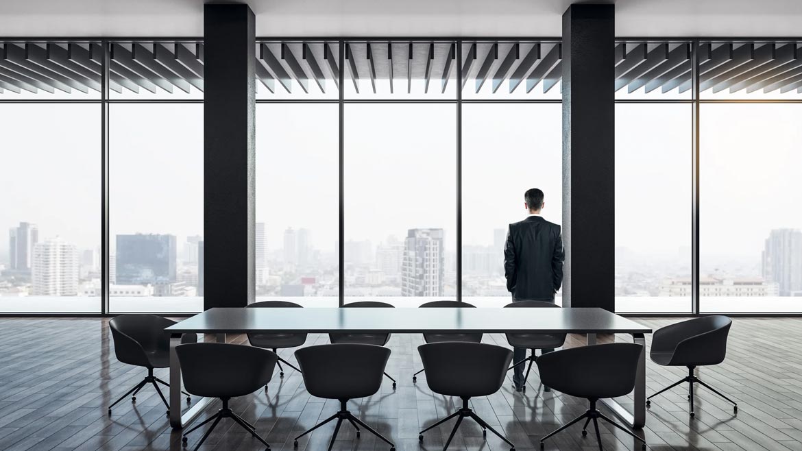 Businessman in front of an empty conference table, looking out of the window.