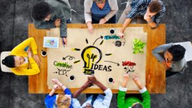 Group of people around a table writing ideas on large pieces of paper.