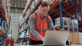 Male worker working on his laptop in a warehouse.