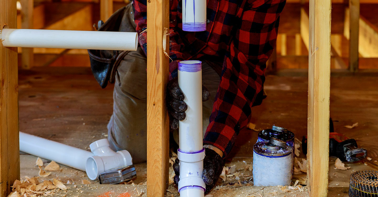 Plumber installing primer and glue PVC pipe at construction home.