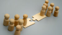 Two groups of wooden figures stand on opposite sides of a puzzle piece bridge.