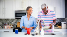 Senior black couple doing dishes in the kitchen and smiling.